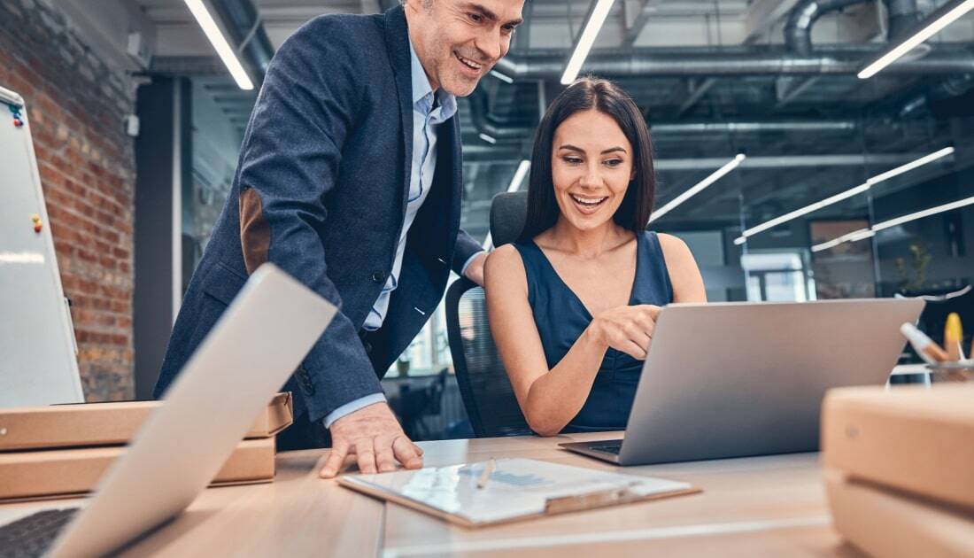 Two professionals in a modern office reviewing data on a laptop, discussing Intelligent Document Processing for efficient document management.