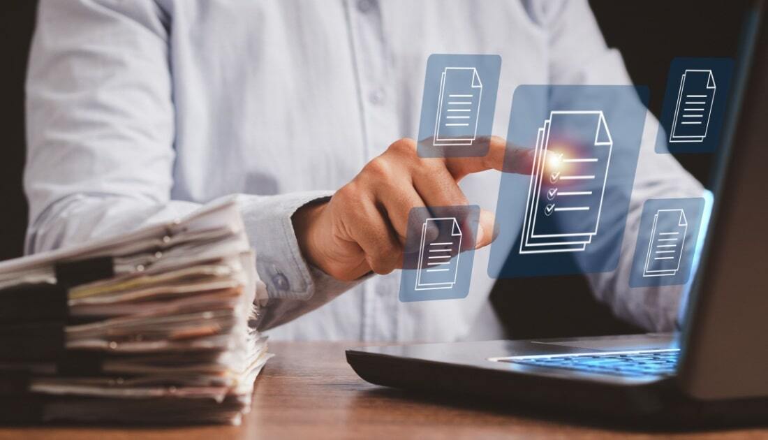 A person organizing digital files on a laptop with floating document icons, representing document indexing strategies for compliance and the shift from paper records to structured digital systems.