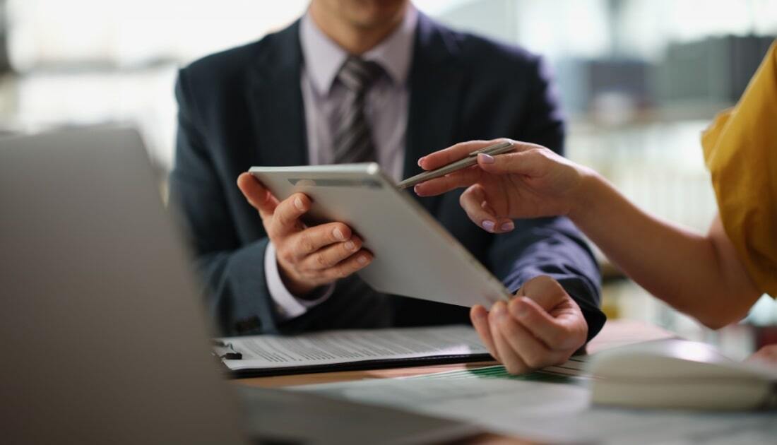 Business professionals reviewing digital files on a tablet during a meeting, illustrating the importance of document control in managing and verifying records.