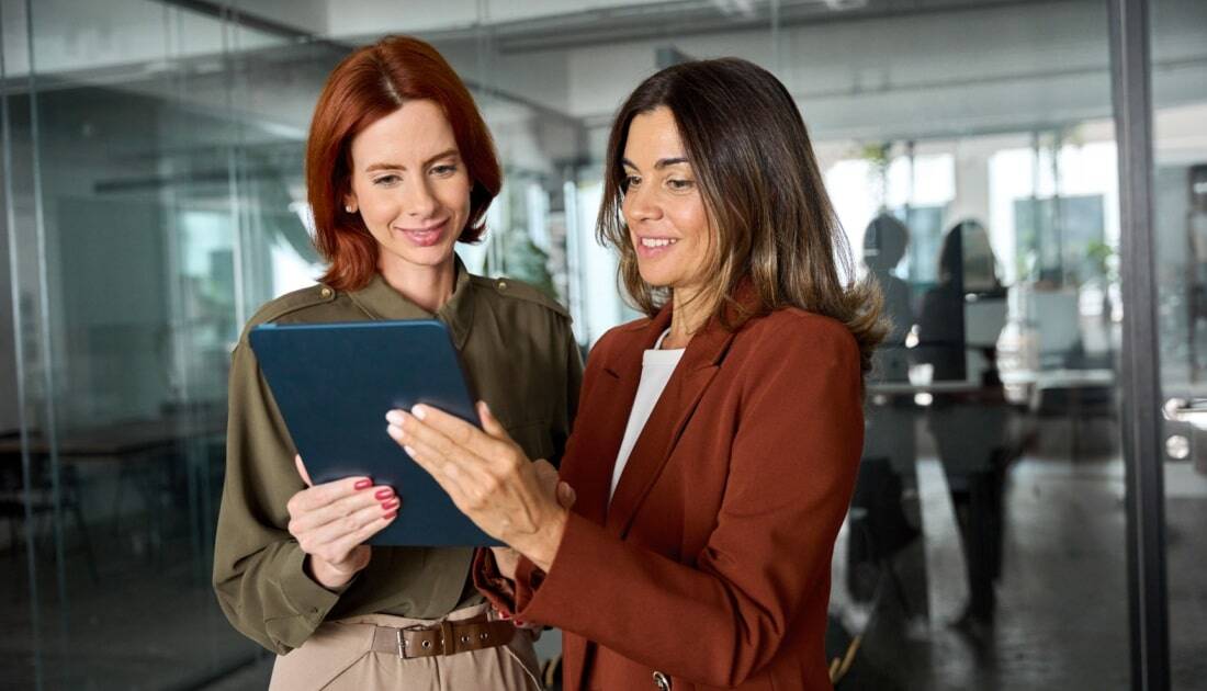 Two happy busy business women talking using tablet