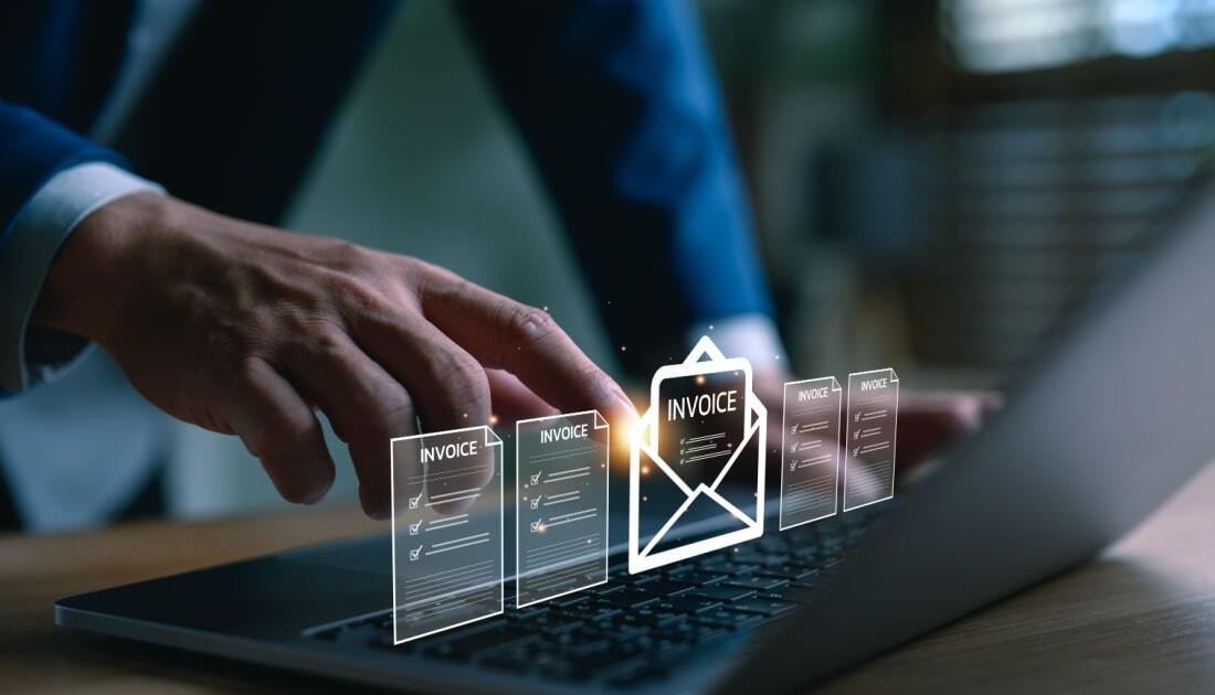 A business professional using a laptop with digital invoice icons floating above the keyboard, representing automated invoicing and accounts payable programs in a modern office setting.